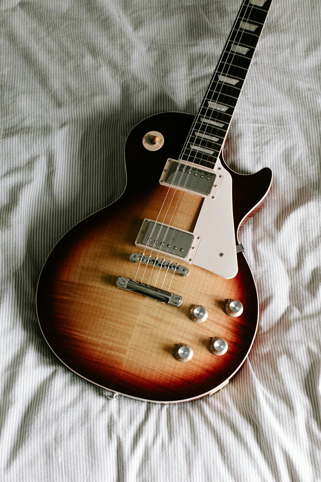 Una guitarra es un clásico objeto de contratos al ser un bien que se puede prestar, vender, comprar o rentar. Foto de una Les Paul Sunburst sobre sábanas rayadas.
