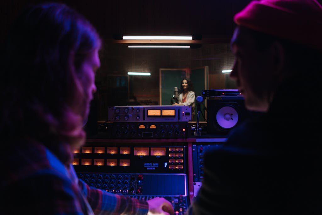 Music studio scene with engineers at mixing console and a singer in the vocal booth. This creates masters.