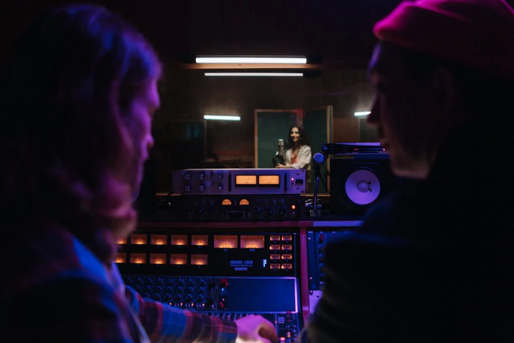 Music studio scene with engineers at mixing console and a singer in the vocal booth. This creates masters.