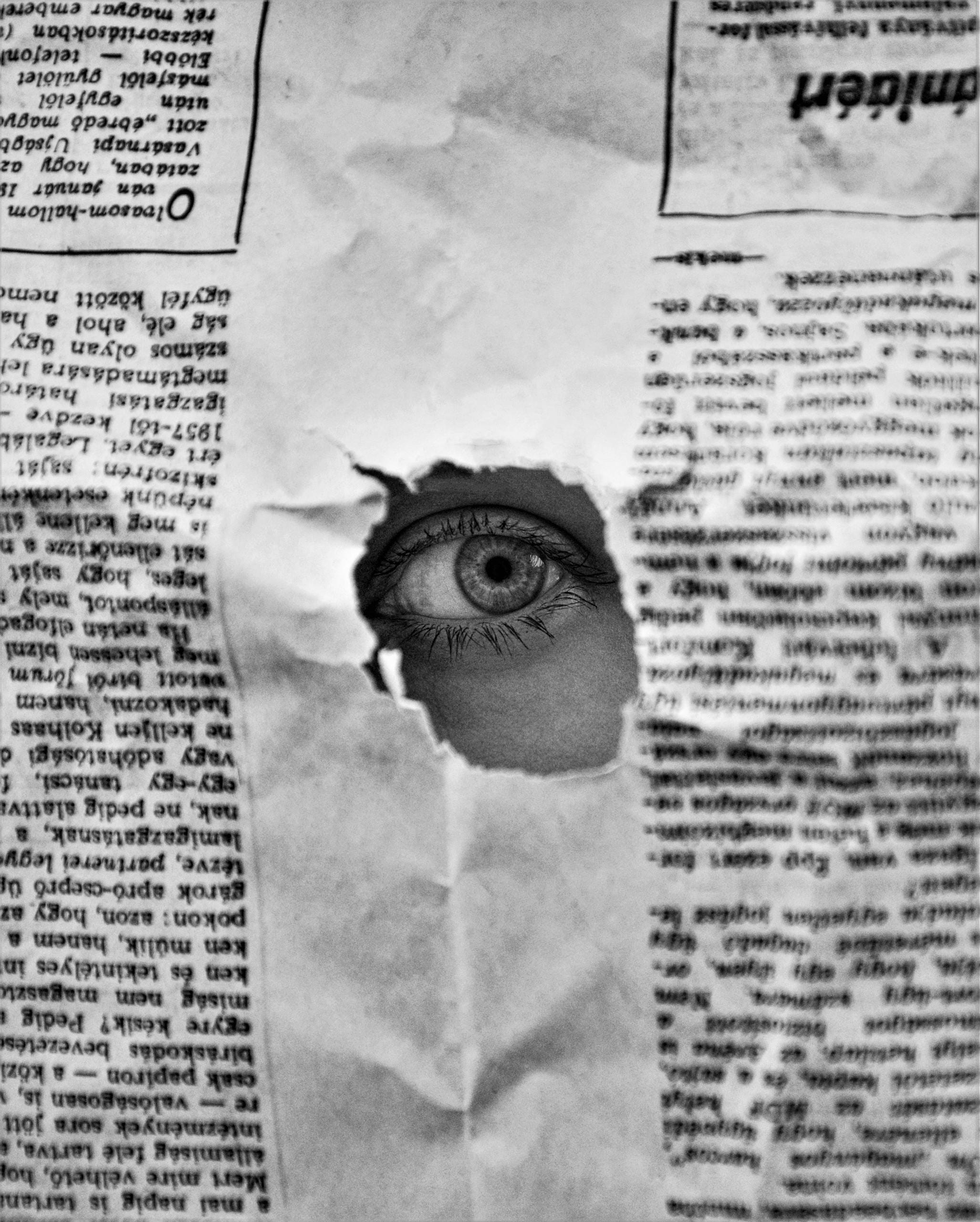 A mysterious eye peering through a hole in a black and white newspaper, creating an intriguing visual.
