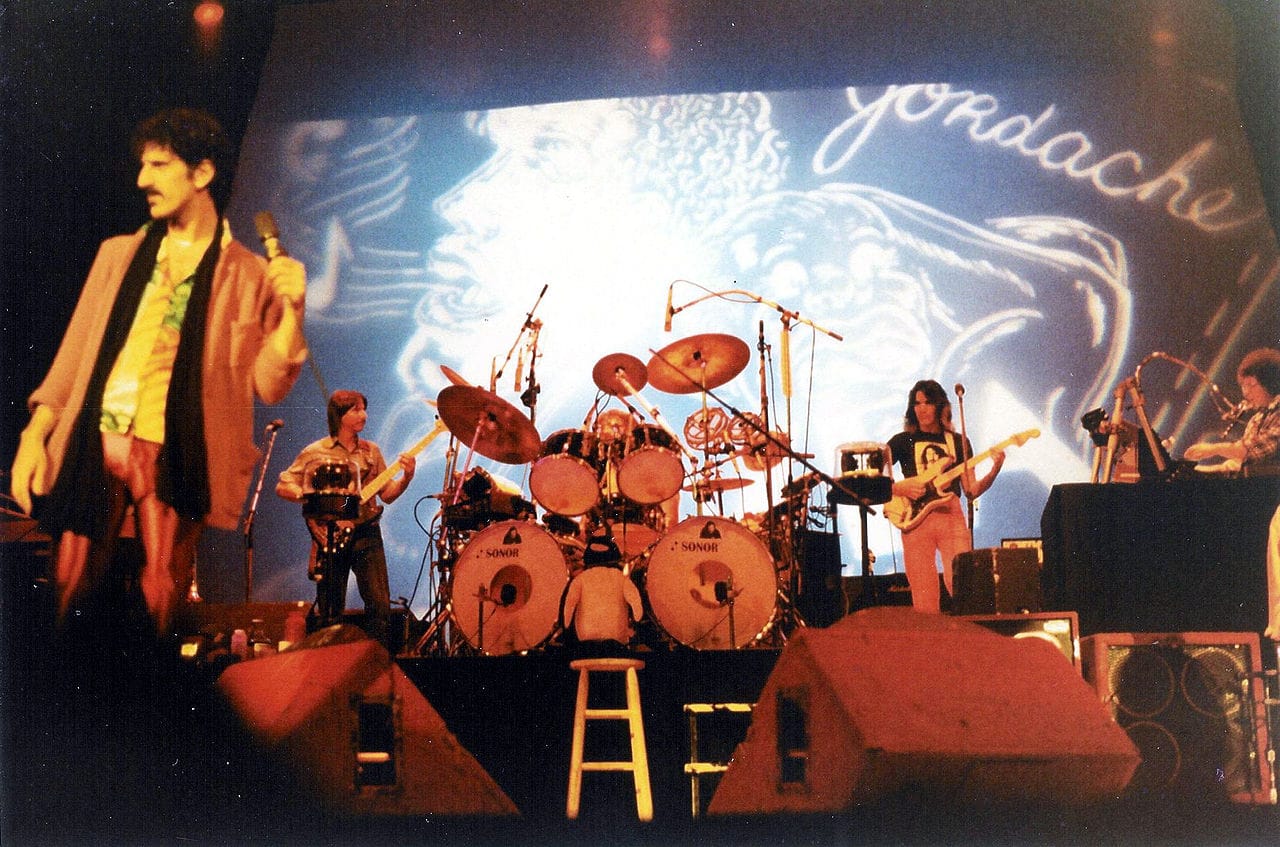 Steve Vai (on guitar in between the drums and keyboard, to the right), Frank Zappa and band during a concert at the Memorial Auditorium in Buffalo, New York (October 25, 1980)